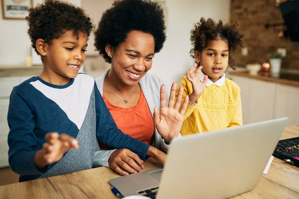 Happy African American mother and her kids waving during video call over laptop at home.