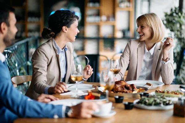 Happy business colleagues drinking wine and talking while eating in a restaurant.