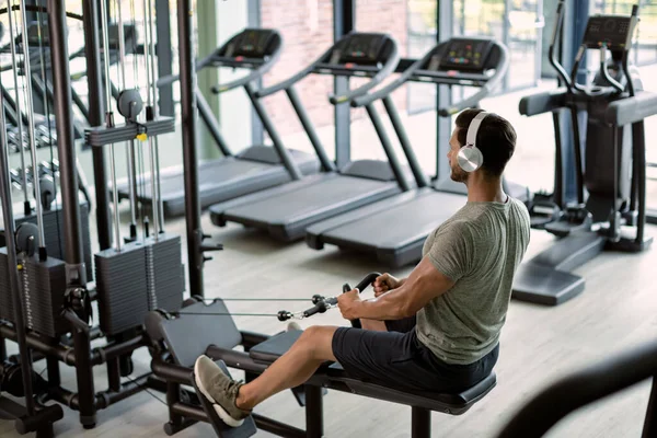 Athletic Man Headphones Exercising Rowing Machine Gym — 图库照片