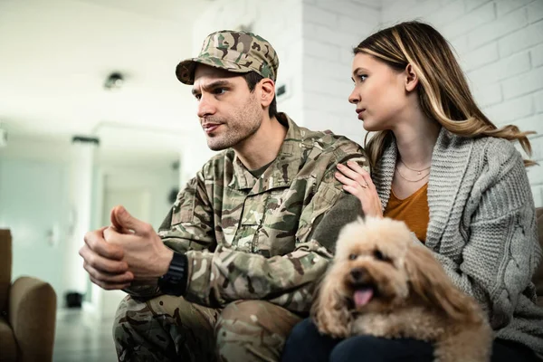 Young distraught military couple with a dog at home. Woman is consoling her husband while he is about to leave for deployment.