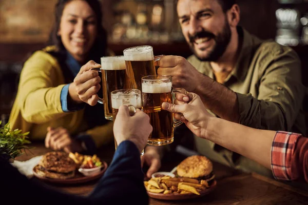 Close-up of group of friends toasting with beer while eating in a pub.