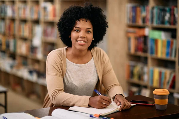 Happy African American mid adult student learning in a library and looking at camera.