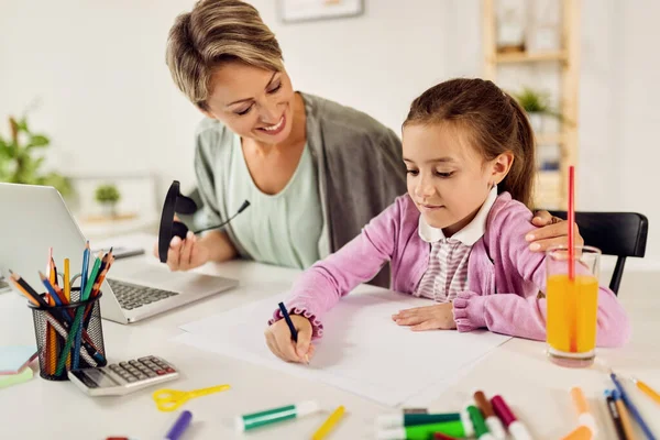 Small girl writing on the paper while learning with her mother at home. 