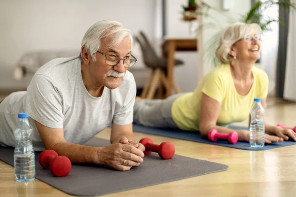 Mature man and his wife working out on the floor at home. 