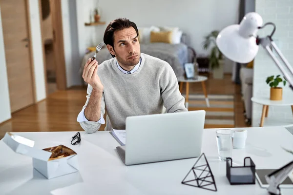 Young Freelance Worker Thinking Something While Working Laptop Eating Home — Stockfoto