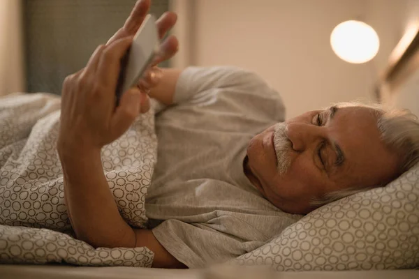 Mature Man Lying Bed Using Mobile Phone Evening — Φωτογραφία Αρχείου