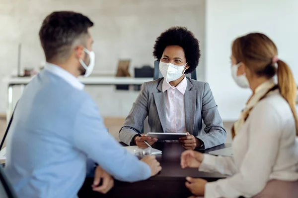 Happy African American financial consultant and her clients wearing protective face masks while having a meeting in the office.