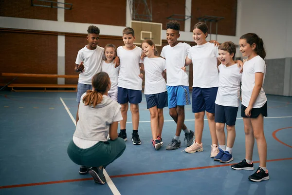 Group of happy elementary students with physical education teacher during a class at school gym.