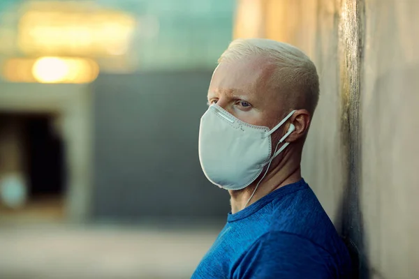 Athletic albino man wearing a face mask and looking away while exercising in the city.