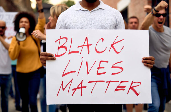 Unrecognizable black man protesting with multi-ethnic group of people and holding Black Lives Matter placard. 