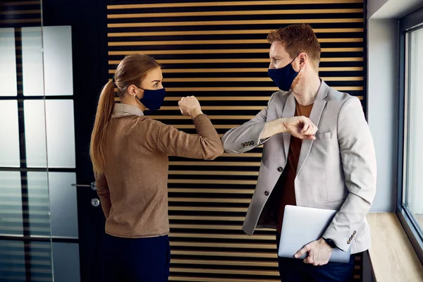 Business colleagues with face masks greeting with elbows while meeting in the office.