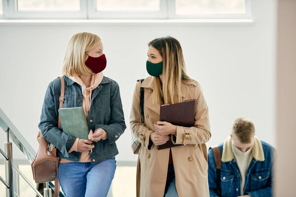 Счастливые подруги общаются в защитных масках и ходят по университетскому коридору. 