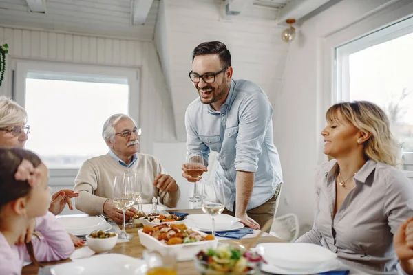 Happy man holding a glass of wine and proposing a toast while having lunch with his extended family in dining room.