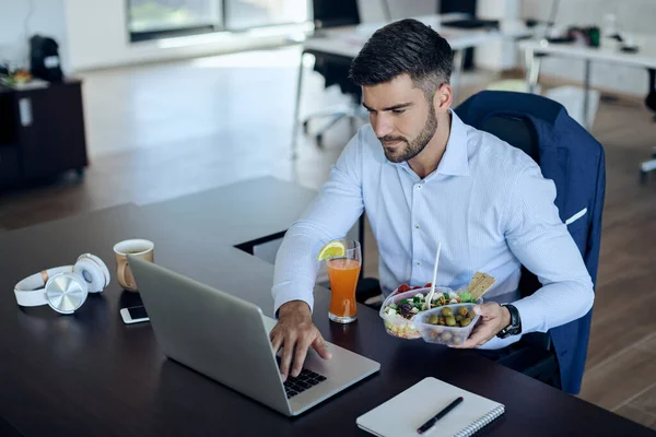 Young businessman surfing the net on computer while eating healthy food in the office.