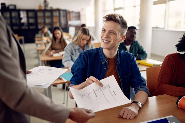 Young happy student receiving exam results from his professor in the classroom.