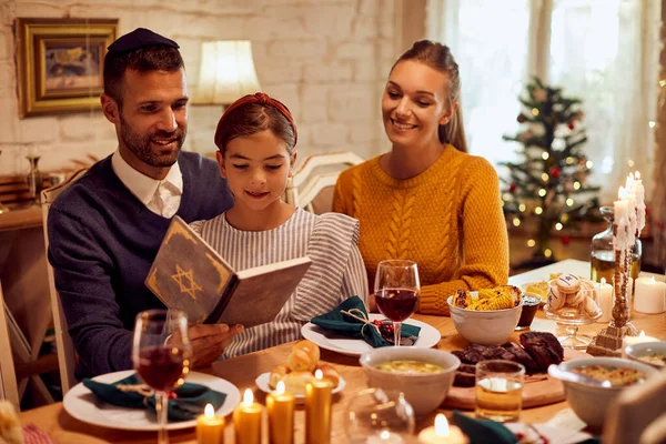 Happy Jewish family reading Tanakh while having meal at dining table on Hanukkah.