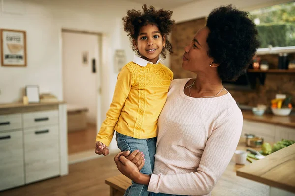 Happy black mother holding her daughter at home. Girl is looking at camera.