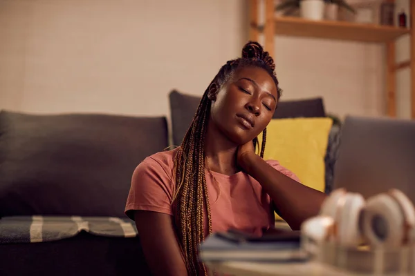 Young tired black student relaxing with her eyes closed after using laptop and learning at night at home.