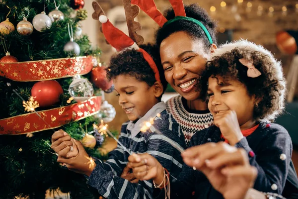 Playful black mother and kids having fun with sparklers on Christmas day at home.