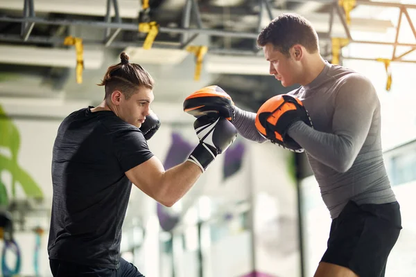 Dedicated fighter exercising with a coach during sports training at the gym.