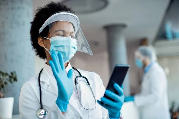 African America Female Doctor Using Mobile Phone Waiving While Having 免版税图库照片