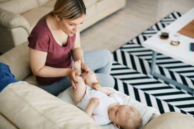High angle view of baby boy relaxing on the sofa while mother is talking to him at home.