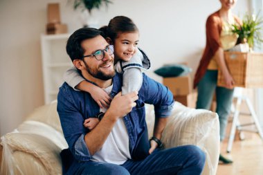 Happy father and daughter embracing after moving into a new house. The mother is in the background. 