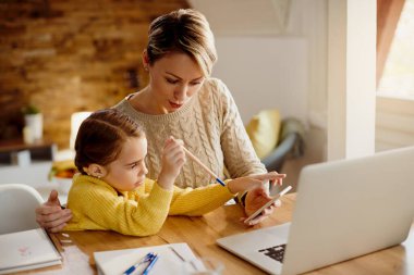Small girl using smart phone with her mother who is working at home.