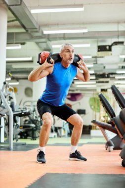 Mature athlete exercises squats while holding sandbag on his sho