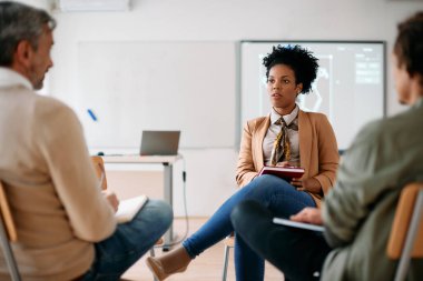 Black female professor having consultations with adult students at lecture hall.