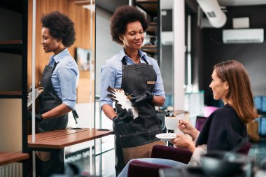 Happy black hairstylist talking with her customer about hair colors while working at hair salon.