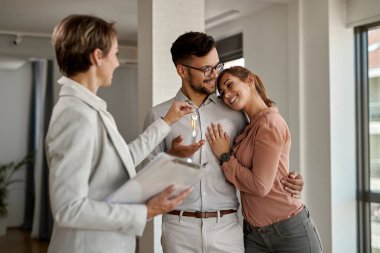 Young happy couple receiving keys of their new home from real estate agent.