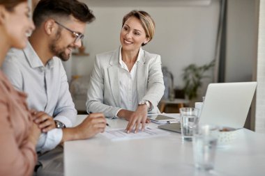 Happy real estate agent and young couple signing an agreement during the meeting. 