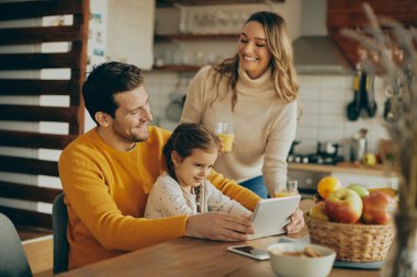Happy father and daughter using touchpad while mother is serving them glass of orange juice at home. 