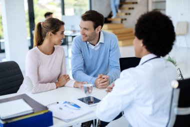 Happy couple having consultation with a doctor and talking to each other at medical clinic. 