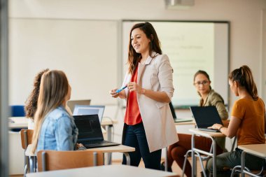 Happy computer science teacher communicating with her students during IT class in the classroom.