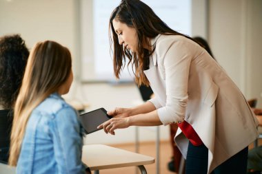 Computer science teacher assisting her student in using digital tablet during computer class at high school. 