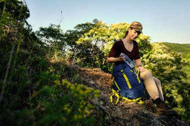 Genç bir kadın ormanda yürürken sırt çantasından su şişesi alıyor.. 