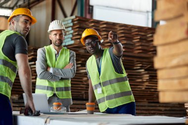 African American warehouse worker and his colleague explaining something to their with inspector during a meeting at lumber department.