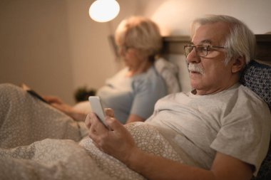 Üst düzey bir adam gece karısıyla yatak odasında yatarken akıllı telefondan internette sörf yapıyor.. 