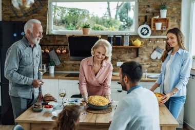 Mutlu çok nesilli aile yemek odasında öğle yemeği yiyor. Spagetti servisi yapan olgun bir kadına odaklan.. 