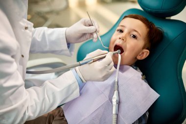 Little boy having his teeth checked by dentist at dental clinic and looking at camera. 