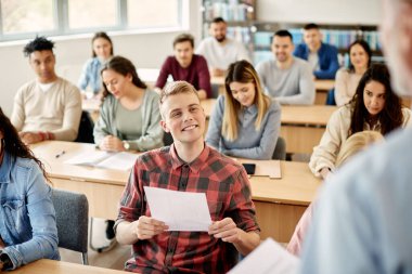 Happy college student feeling satisfied with his exam results and communicating with his teacher in the classroom. 