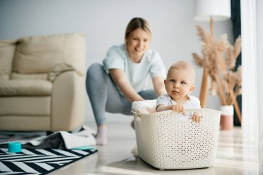 Playful mother having fun with her small son who is sitting in white basket. Focus is on baby boy. 
