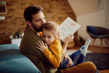 Affectionate father kissing his daughter after receiving a drawing from her at home.