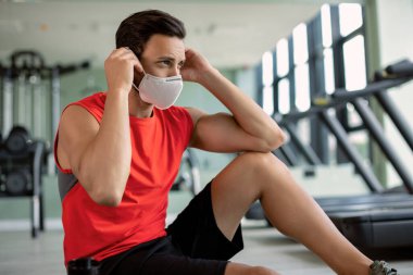 Athletic man preparing for workout and putting on protective face mask in a health club due to coronavirus epidemic. 