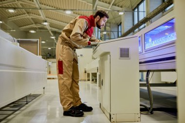 Full length of factory worker working on automated production line machine at woodworking facility. 