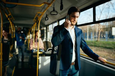 Businessman communicating over mobile phone while traveling by public bus to work.
