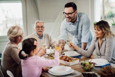 Happy extended family toasting while having lunch in dining room. Focus is on mid adult man toasting with is daughter. 