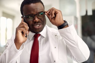 African American doctor using mobile phone and making a phone call while working at medical clinic. 